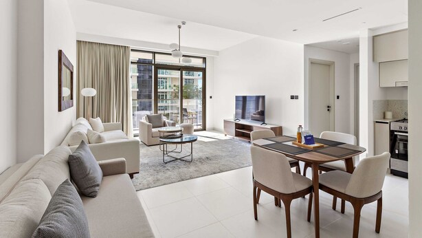 Ein modernes Wohnzimmer mit Sofa, Sesseln, Esstisch und Fernseher.