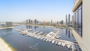 A marina with numerous boats docked, a city skyline in the background, and a clear sky. - Silkhaus Spacious 2BR Marina Vista Tower Beach (Dubai)
