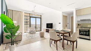 A modern living room with a dining area, a large plant, a TV, and a kitchen with an oven. - Silkhaus Luxurious 1bdr With Sea View in Emaar (Dubai)