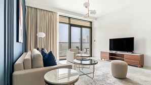A modern living room with a sofa, round coffee table, ottoman, and a TV on a wooden cabinet. - Silkhaus Luxurious 1bdr With Sea View in Emaar (Dubai)
