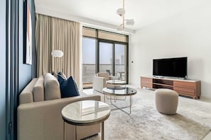 Ein modernes Wohnzimmer mit einer Couch, einem runden Couchtisch, einem Hocker und einem Fernseher auf einer Holzkommode.