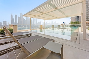 A rooftop pool area with sun loungers and a glass railing overlooking a city skyline. - Silkhaus Luxurious 1bdr Sunset Sea View (Dubai)