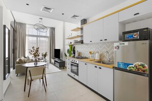A modern kitchen with a built-in oven, microwave, and refrigerator. There is a dining area with a table and chairs, and a sofa in the background. - Silkhaus Socio Tower Dubai Hills Neighborhood (Dubai)
