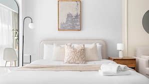 A neatly made bed with white linens and decorative pillows, a bedside table with a lamp, and a framed artwork on the wall. - Silkhaus Stylish Studio Nova Tower in DSO (Dubai)