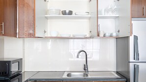 A kitchen with wooden cabinets, a stainless steel sink, and a microwave. - Silkhaus Stylish Studio Nova Tower in DSO (Dubai)