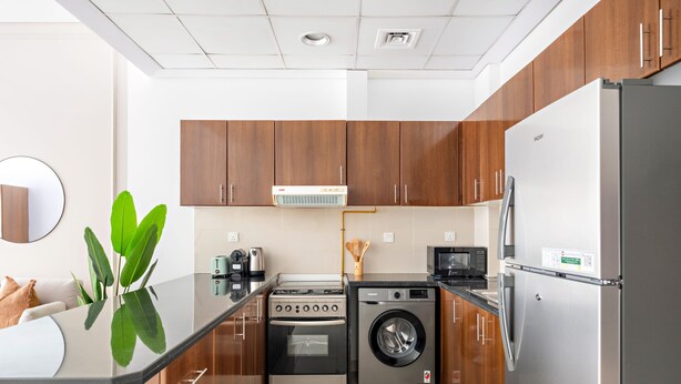 A modern kitchen with wooden cabinets, a stainless steel refrigerator, a washing machine, and a microwave. - Silkhaus Stylish Studio Nova Tower in DSO (Dubai)