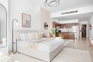 A modern hotel room with a large bed, a bedside table, a floor lamp, and a view into the kitchen area. - Silkhaus Stylish Studio Nova Tower in DSO (Dubai)