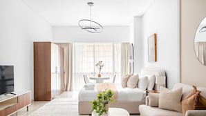 A modern living room with a sofa, a coffee table, a TV, and a large window with curtains. - Silkhaus Stylish Studio Nova Tower in DSO (Dubai)