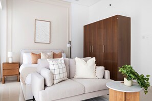 Ein modernes Schlafzimmer mit Schlafsofa, Holzschrank, Nachttisch mit Lampe und einer Topfpflanze.