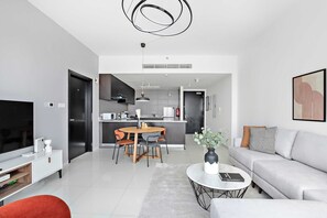 A modern living room with a sofa, TV, and coffee table. There is a dining area with a table and chairs. The kitchen is visible in the background. - Silkhaus Big 1bdr by Al Fay Park Horizon Tower (Abu Dhabi)