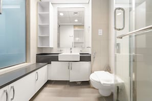 A modern bathroom with a glass shower enclosure, a white toilet, and a vanity with a sink and mirror. - Silkhaus Offshore Studio Palm Views East Tower (Dubai)