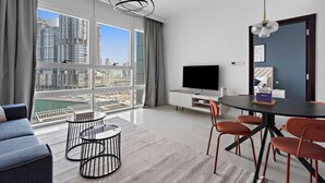 A modern living room with a large window, a flat-screen TV, a dining table with chairs, and a sofa. - Silkhaus Horizon Tower Big 1bdr Near Al Fay Park (Abu Dhabi)