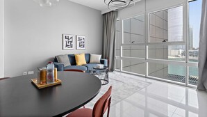 A modern living room with a dining table, sofa, and large windows offering a city view. - Silkhaus Horizon Tower Big 1bdr Near Al Fay Park (Abu Dhabi)