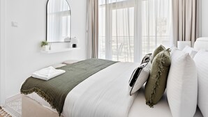 A neatly arranged bedroom with a bed, a bedside table with a lamp, a mirror, and a window with curtains. - Silkhaus Modern 1BR in Oasis Masdar City Park (Abu Dhabi)