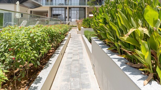 A modern building with multiple floors, large windows, and a central pathway flanked by greenery. - Silkhaus Modern 1BR in Oasis Masdar City Park (Abu Dhabi)