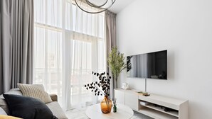 A modern living room with a sofa, a coffee table, a TV, and a large window with curtains. - Silkhaus Modern 1BR in Oasis Masdar City Park (Abu Dhabi)
