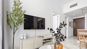 A modern living room with a large flat-screen TV, a minimalist wooden console, a round marble coffee table, and a potted plant. - Silkhaus Modern 1BR in Oasis Masdar City Park (Abu Dhabi)