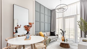 A modern living room with a round dining table, a sofa with cushions, and a coffee table with a vase. - Silkhaus Modern 1BR in Oasis Masdar City Park (Abu Dhabi)