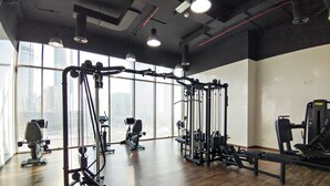 A gym with various exercise equipment, large windows, and a high ceiling. - Silkhaus Horizon Tower 1 BDR Near Al Fay Park (Abu Dhabi)