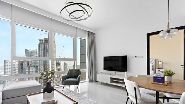 A modern living room with a large TV, dining table, and seating area. - Silkhaus Horizon Tower 1 BDR Near Al Fay Park (Abu Dhabi)