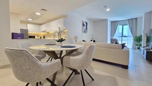 A modern living room with a round dining table, white sofas, and a kitchen in the background. - Silkhaus Serene 1bdr Apartment Al Reem Island (Abu Dhabi)