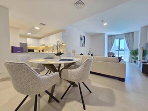 Un salon moderne avec une table à manger ronde, des canapés blancs et une cuisine en arrière-plan.