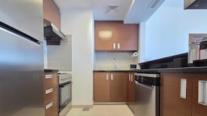A modern kitchen with wooden cabinets, stainless steel appliances, and a tiled floor. - Silkhaus Signature 1BR in Reem Island Gate Tower (Abu Dhabi)