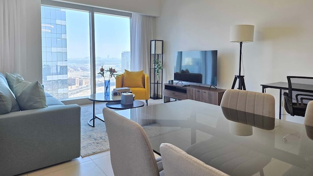 A modern living room with a large flat-screen TV, a dining table, and a sofa. - Silkhaus Signature 1BR in Reem Island Gate Tower (Abu Dhabi)