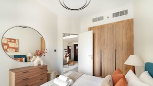 A modern bedroom with a bed, a dresser, a mirror, and a wooden wardrobe. - Silkhaus 1BR Elegant Living In Maryah Vista (Abu Dhabi)