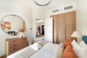A modern bedroom with a bed, a dresser, a mirror, and a wooden wardrobe. - Silkhaus 1BR Elegant Living In Maryah Vista (Abu Dhabi)