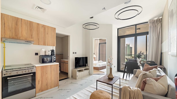A modern apartment with a kitchen, living area, and balcony. It features wooden cabinets, a built-in oven, a flat-screen TV, a sofa, and a dining area. - Silkhaus 1BR Elegant Living In Maryah Vista (Abu Dhabi)