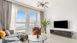 A modern living room with a sofa, armchair, round coffee table, potted plant, TV, and a large window with a view. - Silkhaus Chic 2BR in Horizon Tower Near Beach (Abu Dhabi)