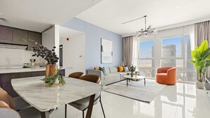 A modern living room with a dining area, a sofa set, and a large window with a city view. - Silkhaus Chic 2BR in Horizon Tower Near Beach (Abu Dhabi)