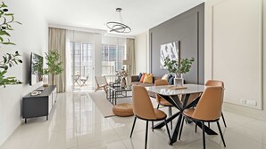 A modern dining area with a round table, chairs, and a chandelier. There is a sofa and a coffee table in the background. - Silkhaus Premier 2BR Stay Near Reem Central Park (Abu Dhabi)