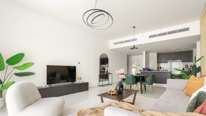 Un salon moderne avec un canapé, une table basse et un téléviseur. On aperçoit à l’arrière-plan un coin repas avec des chaises et une table.