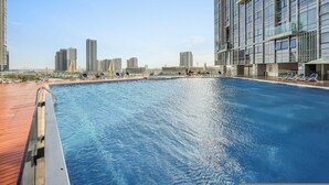 Une piscine sur le toit, avec des chaises longues, et une vue sur les toits de la ville en arrière-plan.