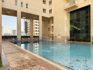 A swimming pool with a tiled deck, a clock, and a lifebuoy on the wall. - Silkhaus New 1bdr Stay at Dubai Production City in Centrium Tower (Dubai)