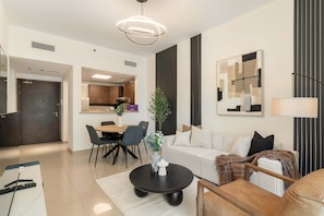 A modern living room with a sofa, coffee table, dining area, and kitchen in the background. - Silkhaus New 1bdr Stay at Dubai Production City in Centrium Tower (Dubai)