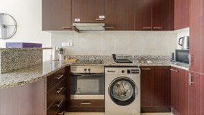 Uma cozinha compacta com forno embutido, micro-ondas e máquina de lavar, armários de madeira e bancada de granito.