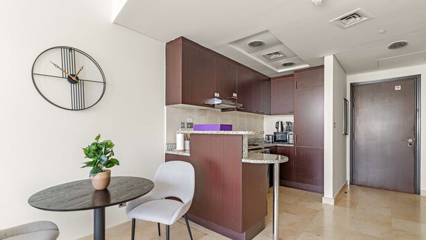 Uma cozinha moderna com uma ilha central, uma área de jantar com mesa redonda e cadeiras, e um relógio de parede grande.