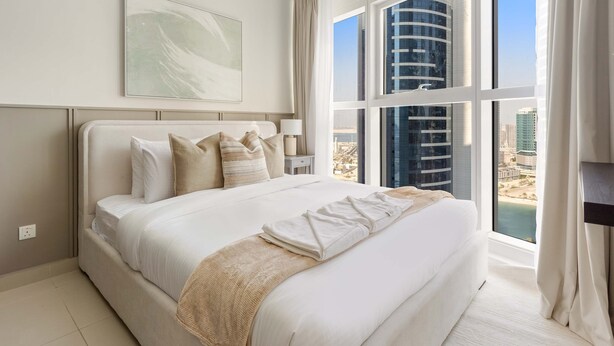 Une chambre d’hôtel moderne avec un grand lit, une vue sur le paysage urbain et un décor minimaliste.