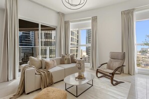 A modern living room with a sofa, coffee table, and armchair, large windows with curtains, and a view of city buildings. - Silkhaus Prestige 2BR Stay in Al Reem Island (Abu Dhabi)