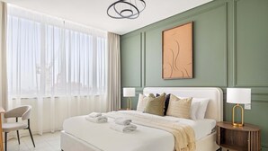A modern hotel room with a large bed, two bedside tables, a chair, and a view of the city through sheer curtains. - Silkhaus Cityscape in Sky Gardens Metro Access (Dubai)