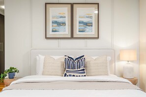A neatly made bed with a white headboard, two framed artworks above, and a bedside lamp on a wooden nightstand. - Silkhaus Exclusive 1bdr Stay Sky Gardens in Difc (Dubai)