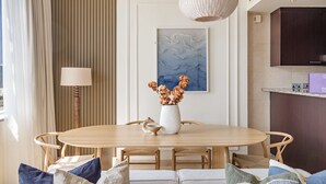 Un comedor con una mesa redonda de madera, sillas, un jarrón con flores, una lámpara y un cuadro en la pared.