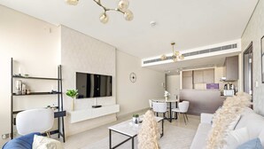 A modern living room with a sofa, coffee table, and TV. There is a kitchen area in the background.