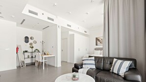 Una sala de estar moderna con un sofá de cuero, una mesa de centro blanca y un comedor con una mesa y sillas blancas.