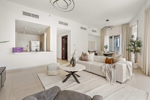 Ein modernes Wohnzimmer mit einem weißen Sofa, einem runden Couchtisch und einem Essbereich im Hintergrund.