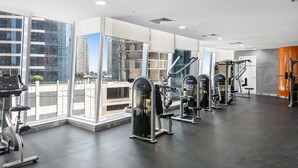Un gimnasio moderno con máquinas de cardio, estaciones de pesas y grandes ventanales con vistas a un paisaje urbano.