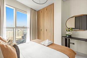 Ein Hotelzimmer mit einem großen Bett, einem Holzschrank, einem Spiegel und Blick auf eine Stadtlandschaft durch große Fenster.